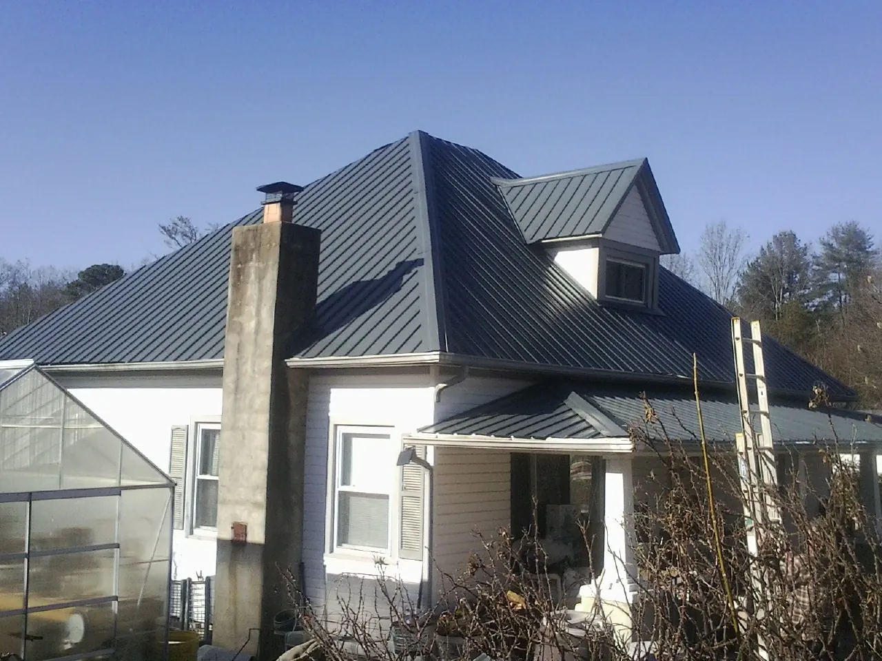 Dark blue standing seam metal roof on a white farmhouse with dormer — Slate & Tile Roof Repair by Roofing Brothers in West Baldwin
