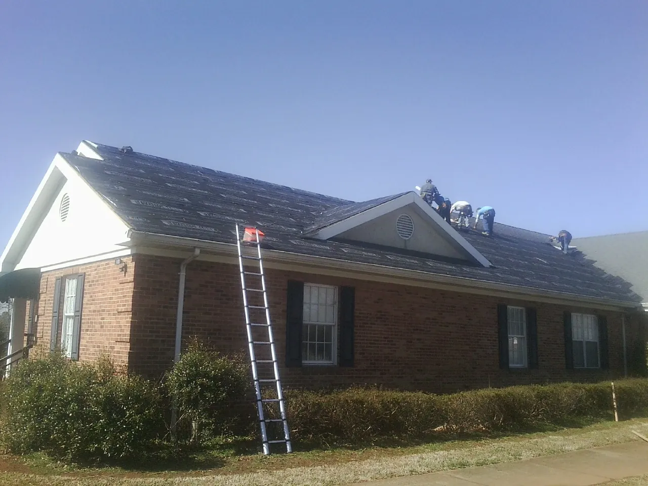 Crew tearing shingles off a brick ranch roof with a ladder set — Emergency Roof Repair work by our crew in West Baldwin
