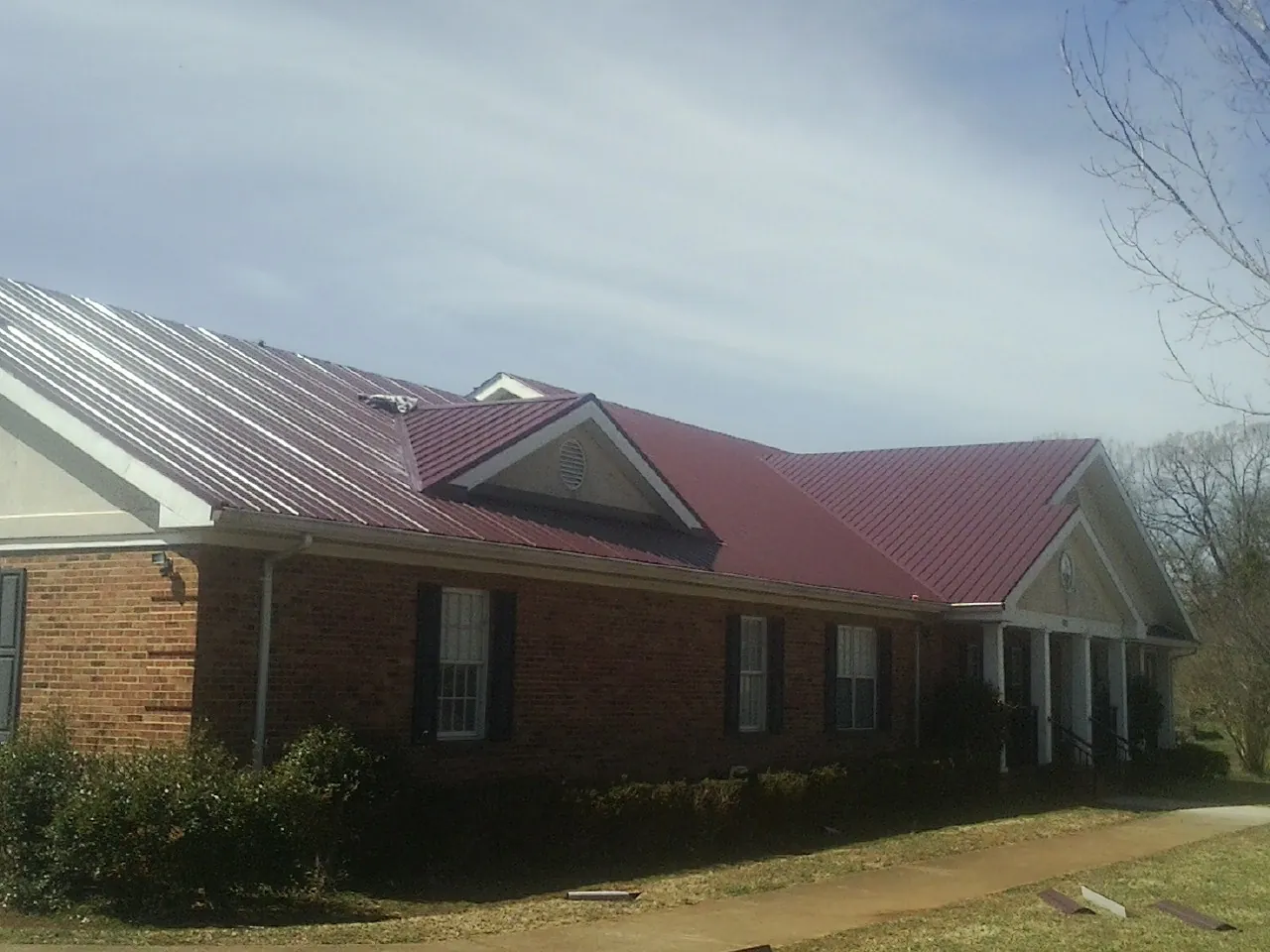 Red metal roof with gabled entries on a long brick building, from a Hail Damage Roof Repair job in West Baldwin