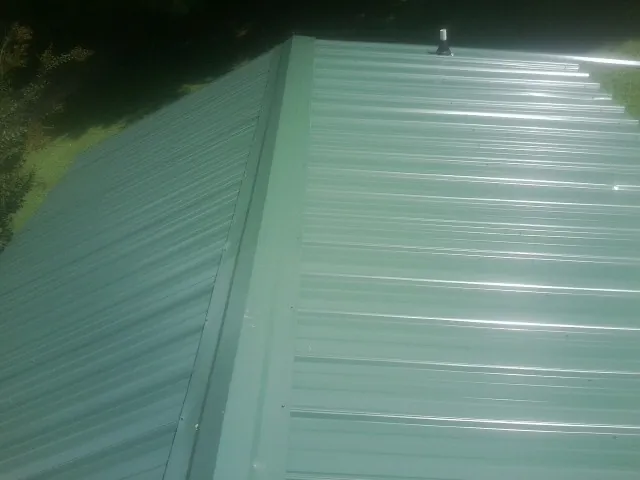 New green metal panels meeting at the ridge of a roof — Flat Roof Repair work by our crew in West Baldwin