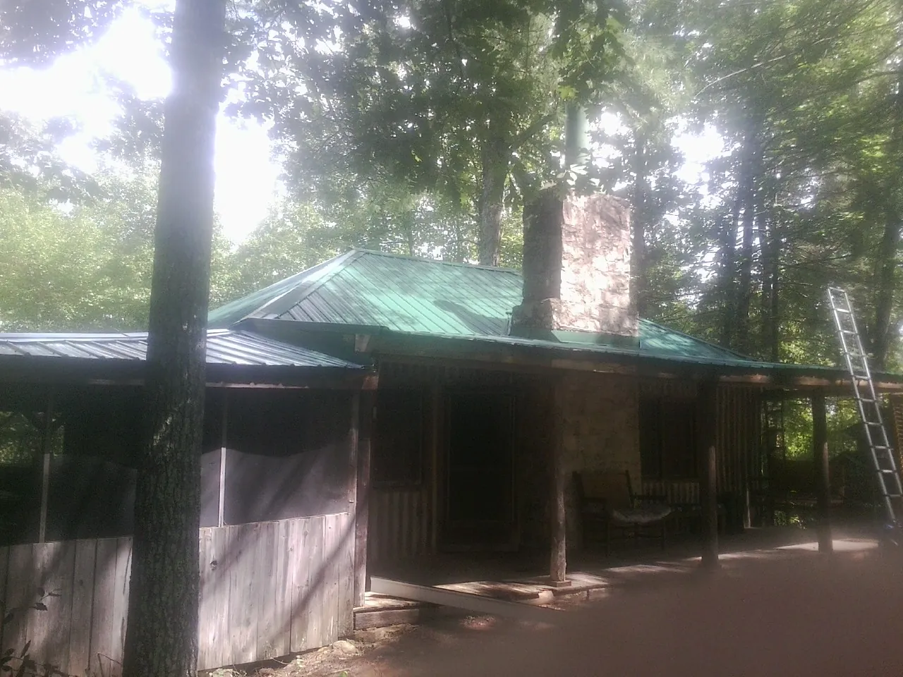 Green metal roof and stone chimney above a log cabin porch in West Baldwin