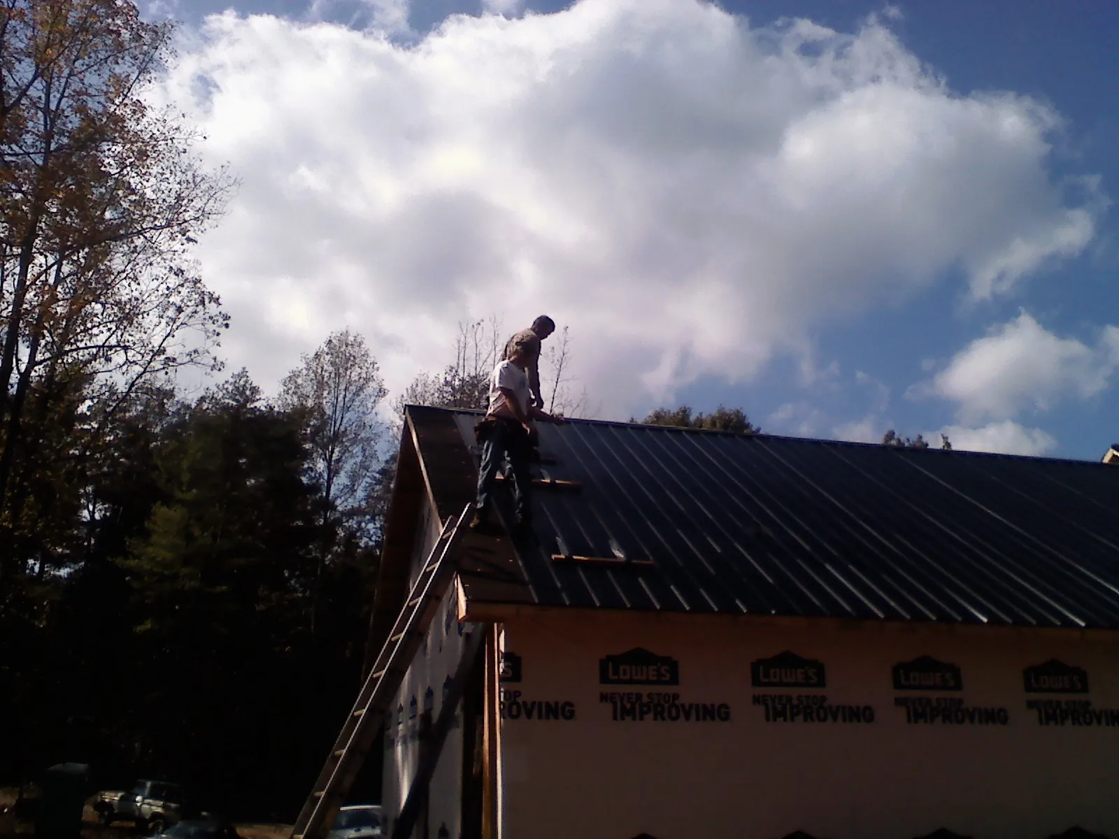 Roofer fastening dark metal panels high against a cloudy sky, from a Roof Inspection job in West Baldwin