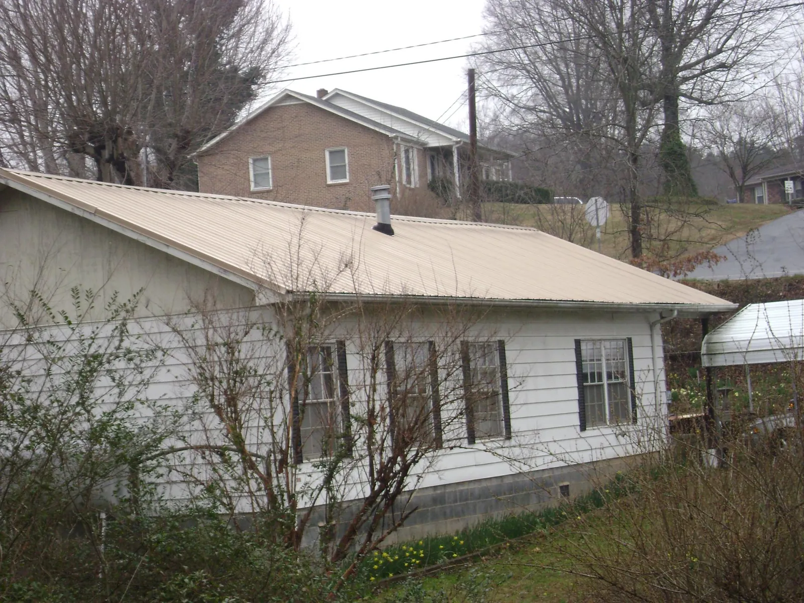 Tan metal roof on a white sided house set into a hillside — Commercial Roofing by Roofing Brothers in West Baldwin